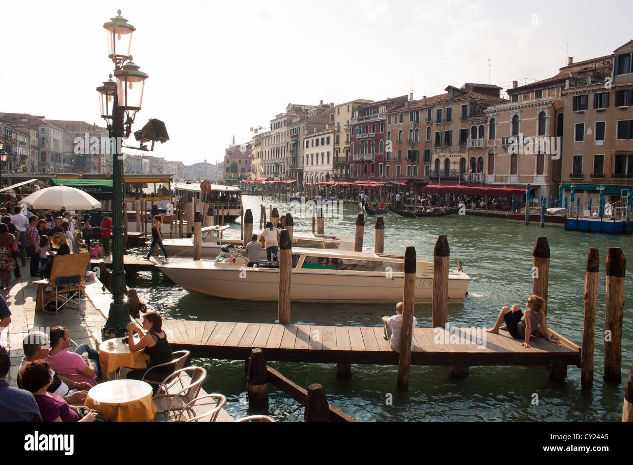 Vista junto al Gran Canal desde el Puente de Rialto; gente sentada en un café y relajarse en un muelle, San Marco, Venecia, Italia Foto de stock