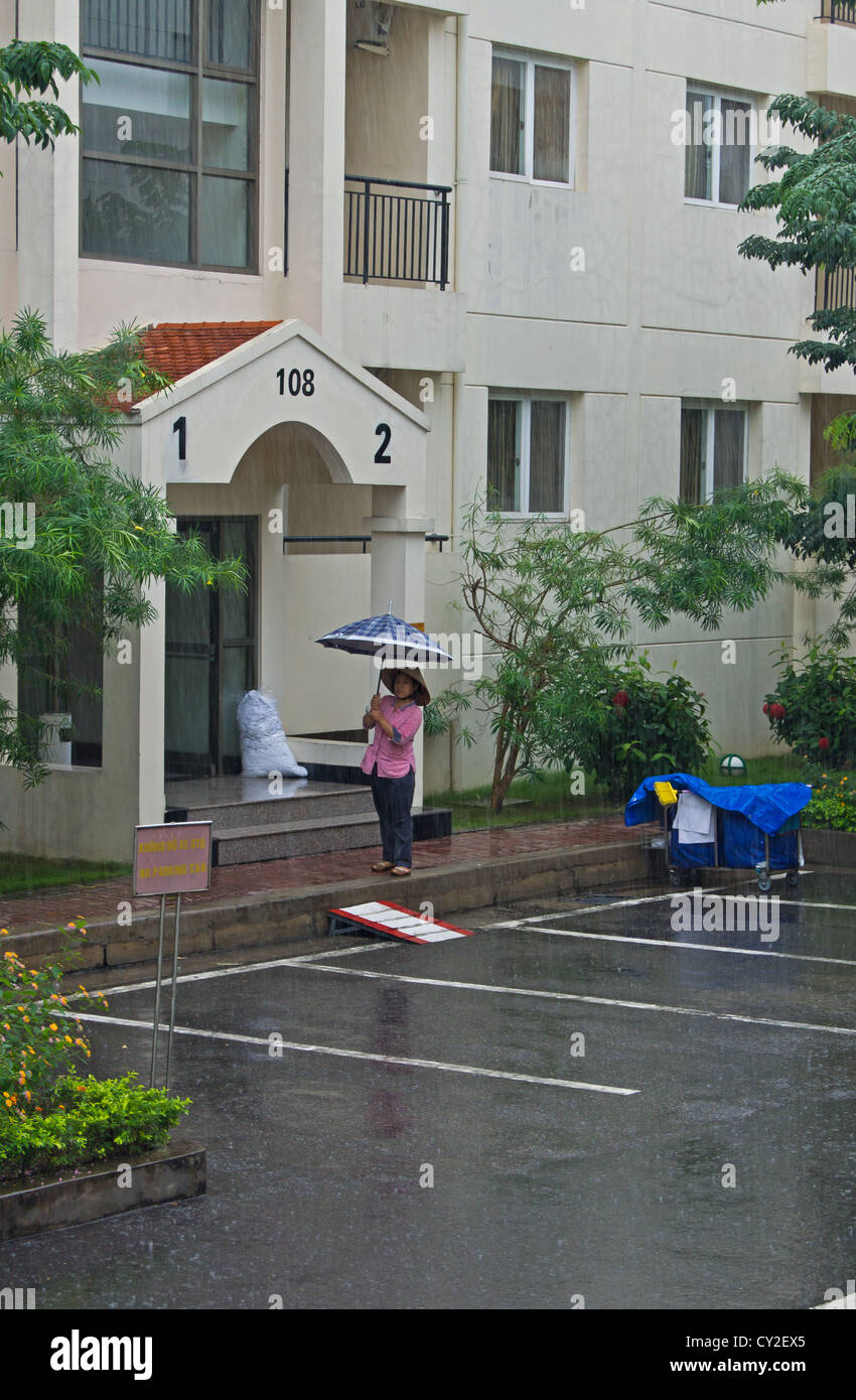 Una criada de pie fuera de las habitaciones en la lluvia Hai Phong Vietnam Foto de stock
