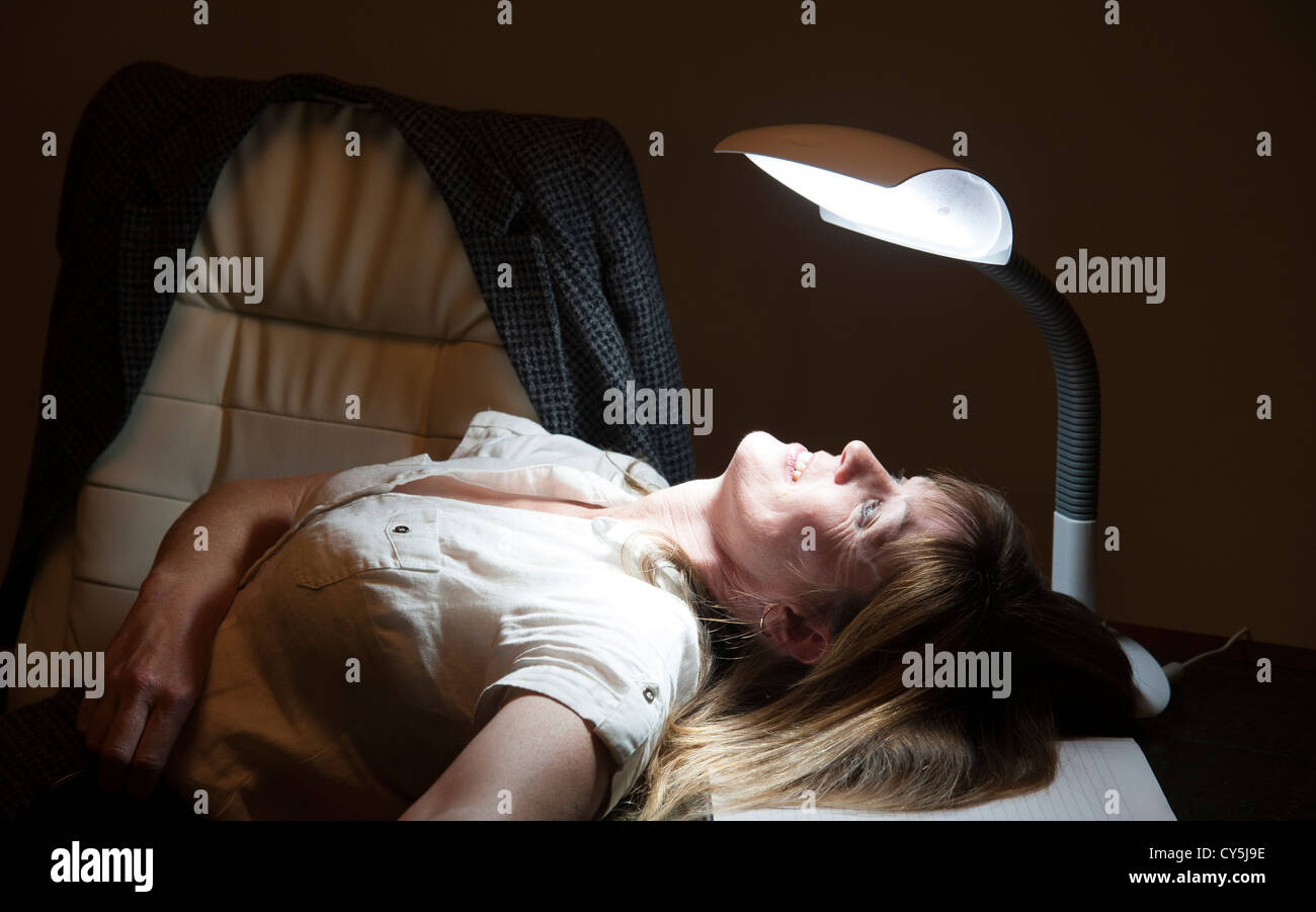 Mujer y triste lámpara de mesa. Trastorno afectivo estacional paciente sentado en el escritorio Foto de stock