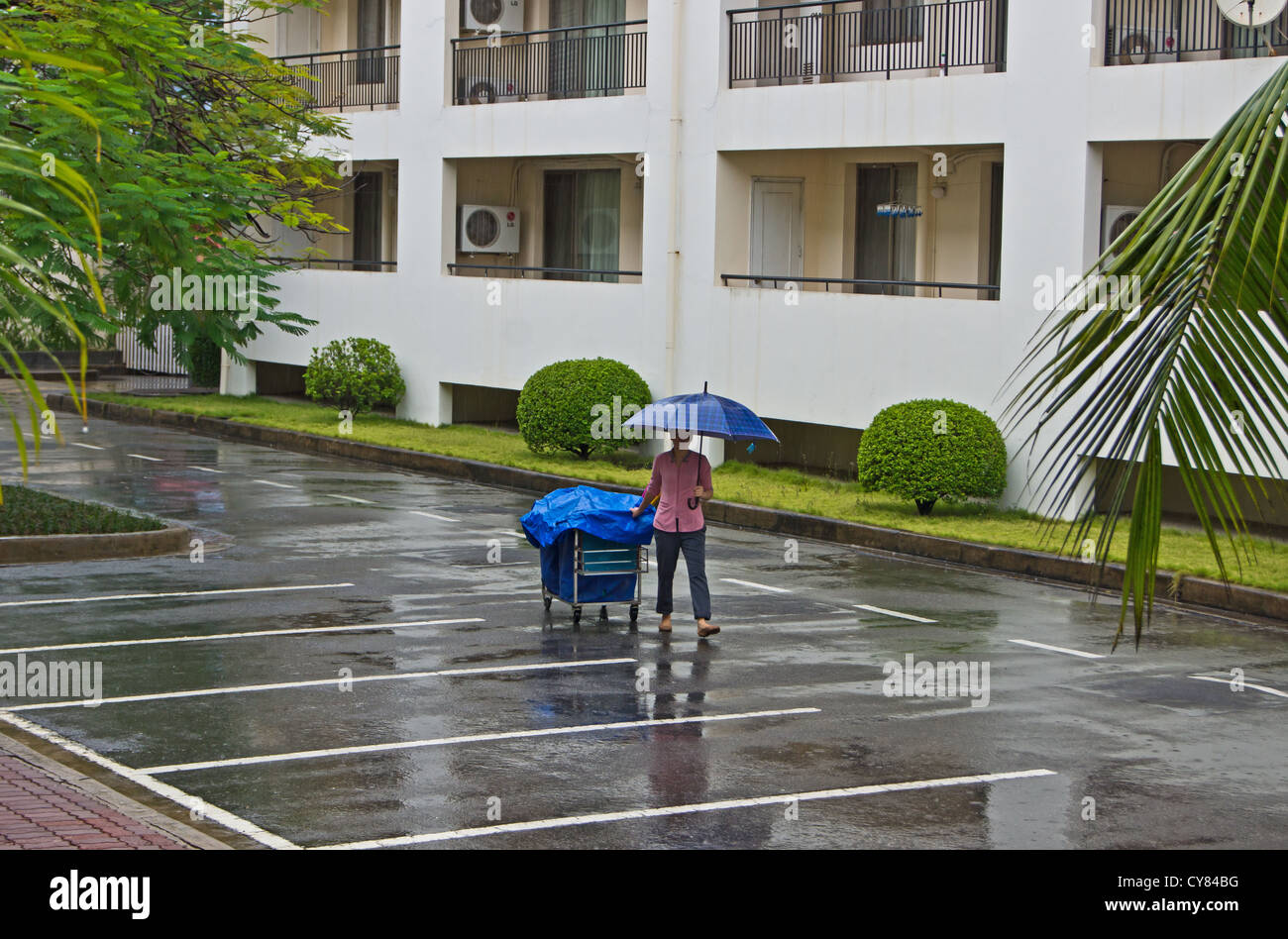 Una criada con su carro en la lluvia caminando a las habitaciones de hotel en Hai Phong Vietnam Foto de stock