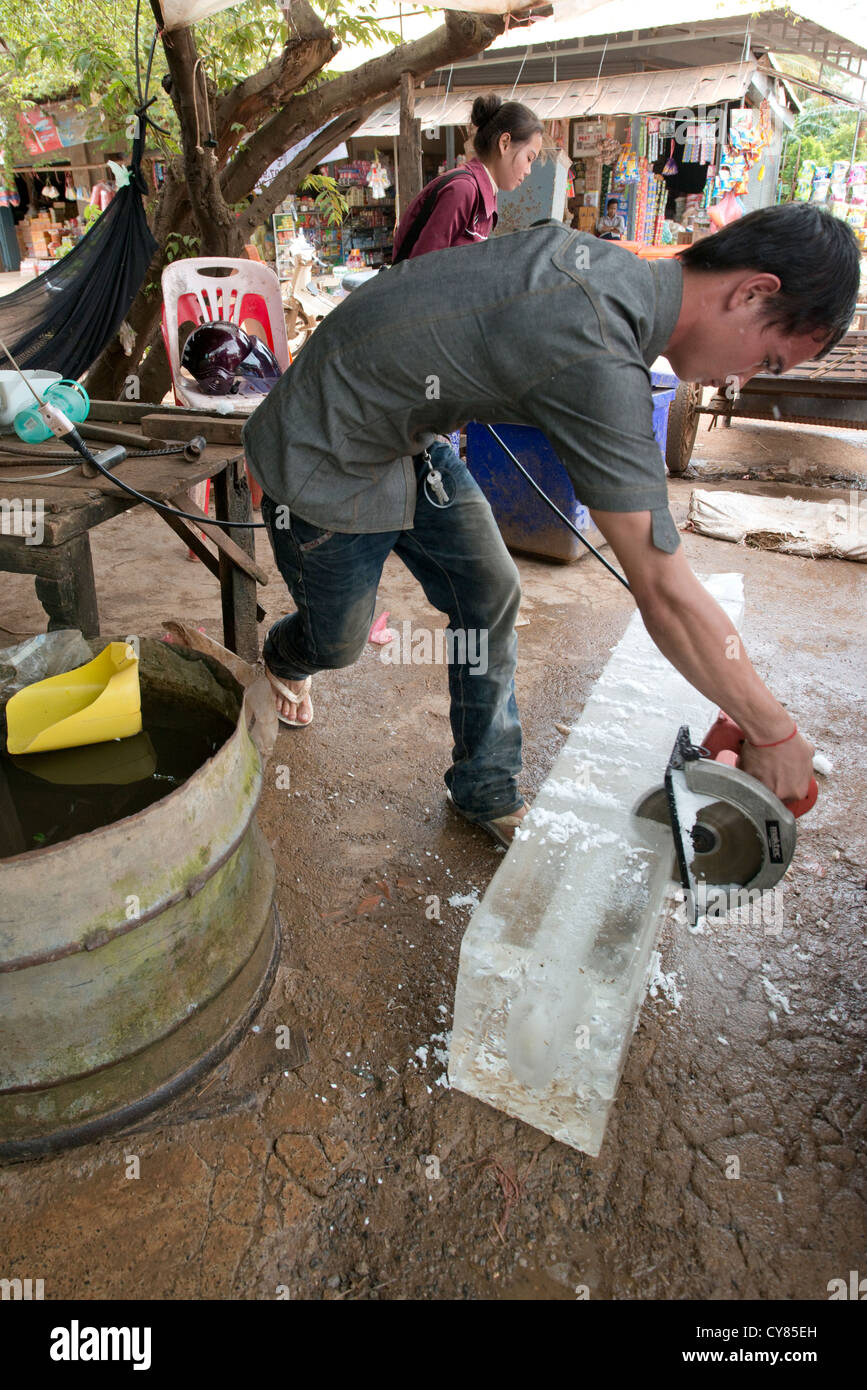 Un comerciante de hielo usa una sierra circular para dividir un bloque grande de hielo en O'Ambel mercado, Sisophon, Camboya Foto de stock