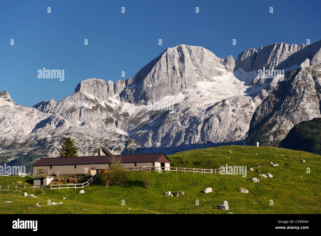 Un pasto de montaña con un granero y altas montañas en el fondo Foto de stock