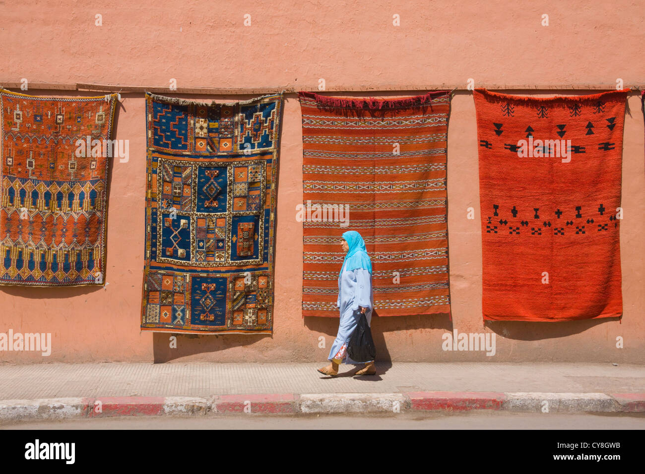 Mujer caminando por tapiz sobre la calle, Marrakech, Marruecos Foto de stock