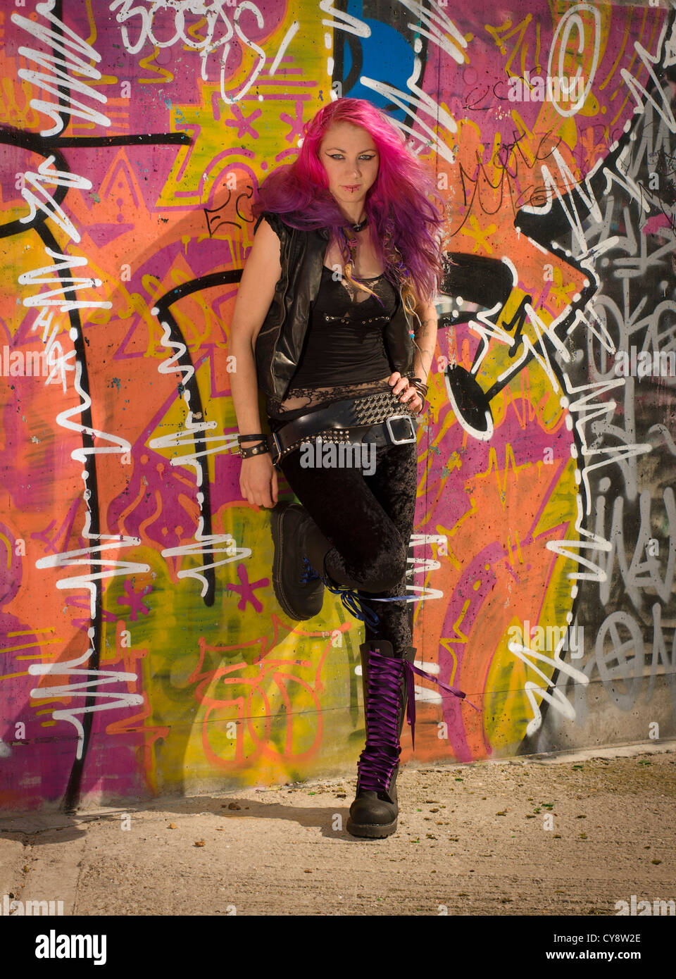 Las mujeres jóvenes/ chica con el pelo rosa y negro chaleco y polainas de  pie delante muro cubierto de graffiti Fotografía de stock - Alamy