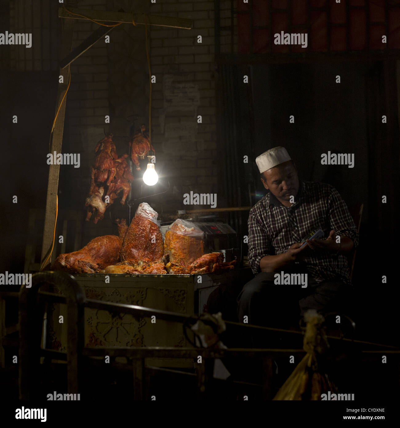 El hombre en su Foodstall uigur en Hotan, mercado nocturno, Región Autónoma Uigur de Xinjiang, China Foto de stock