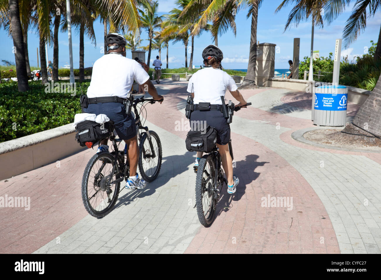 Vista trasera de dos agentes de policía que patrulla en bicicleta a lo largo de paseo, Miami Beach, Florida, Estados Unidos. Foto de stock