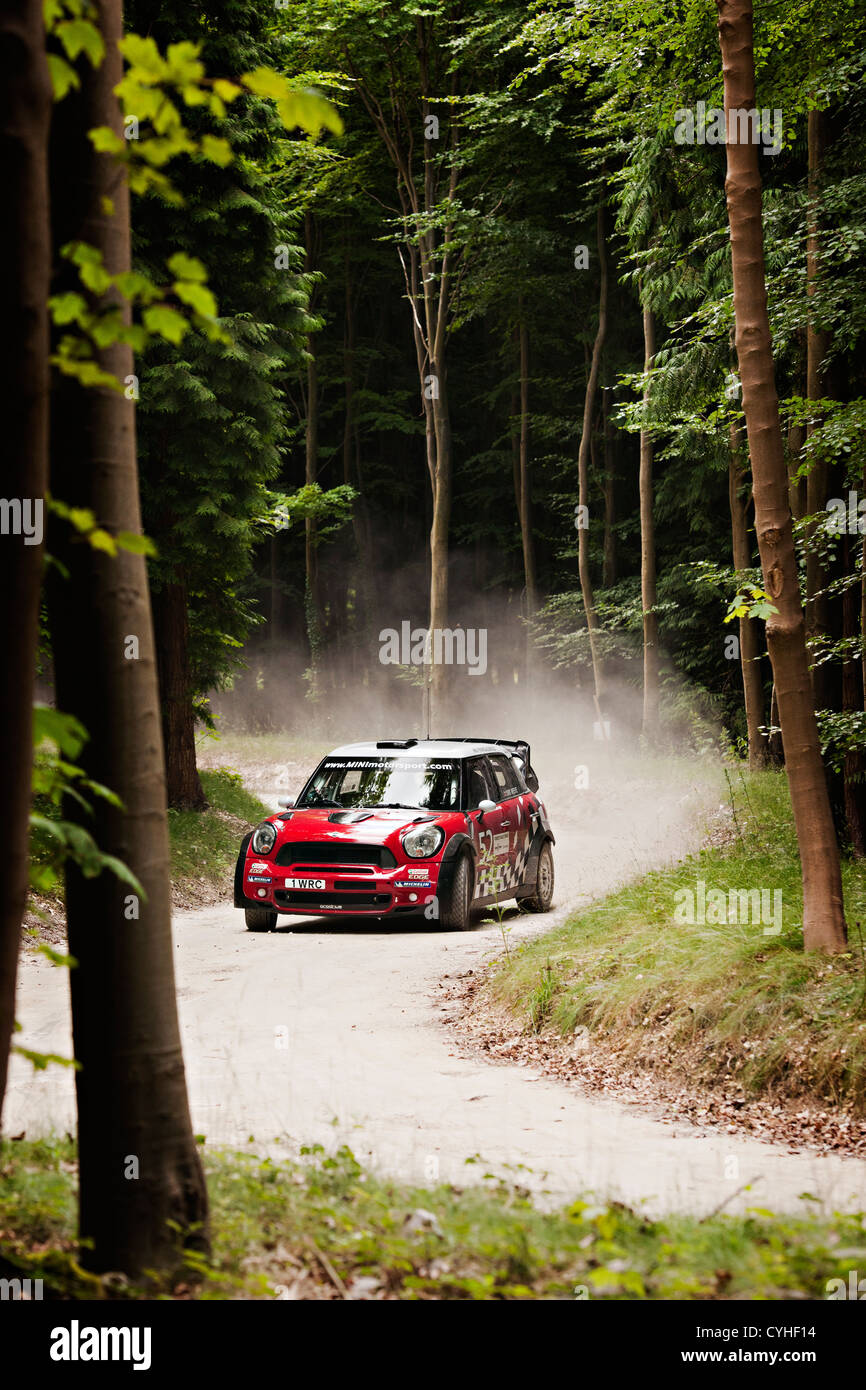 Un rojo WRC Mini Cooper John Cooper Works serpientes alrededor de una estrecha pista forestal arbolada en un circuito de rally Foto de stock