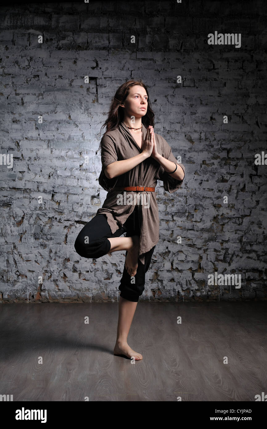 Longitud completa retrato de joven bella mujer haciendo ejercicios de yoga contra una pared de ladrillos Foto de stock