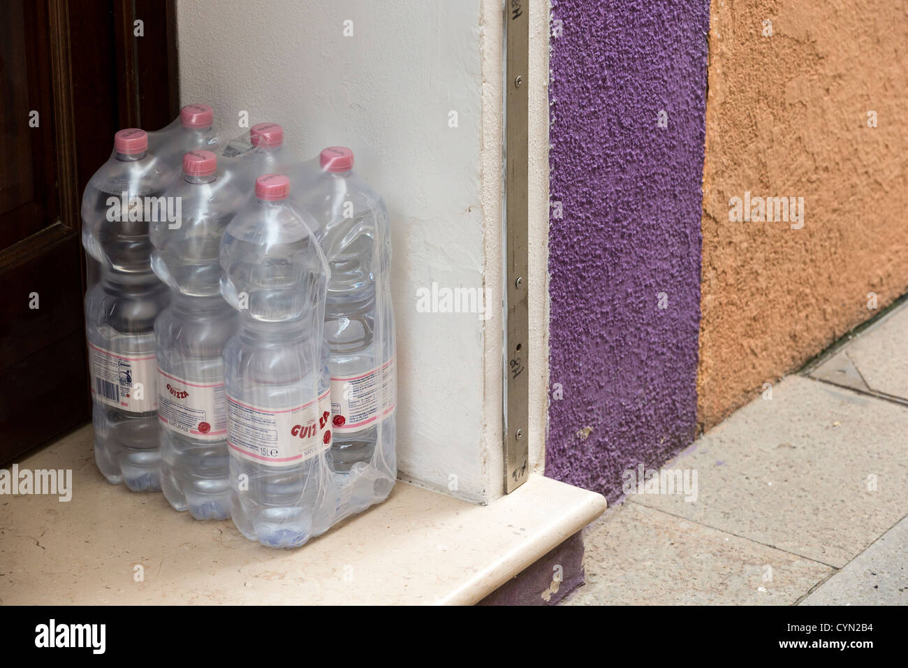 Se empaqueta un paquete de botellas de agua mineral en una puerta blanca con una pared detrás de púrpura y amarillo Foto de stock
