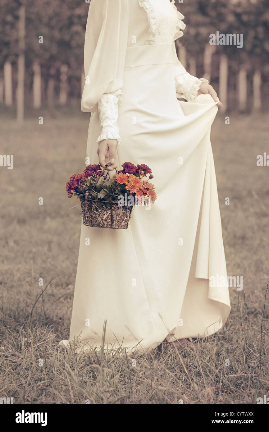 Una mujer en un vestido victoriano está caminando sobre una pradera con una canasta de flores Foto de stock