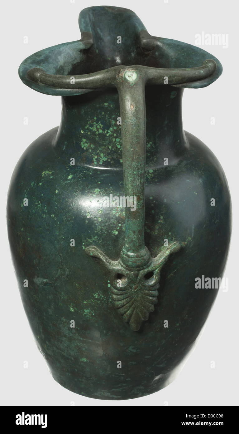 Una jarra etrusca de pico-espumozado, siglo 5 a. C. Bronce con fina pátina  noble verde. Cuerpo con cuello estrecho y boquilla extendida. Mango  remachado, su base en forma de palmeta. Altura 29