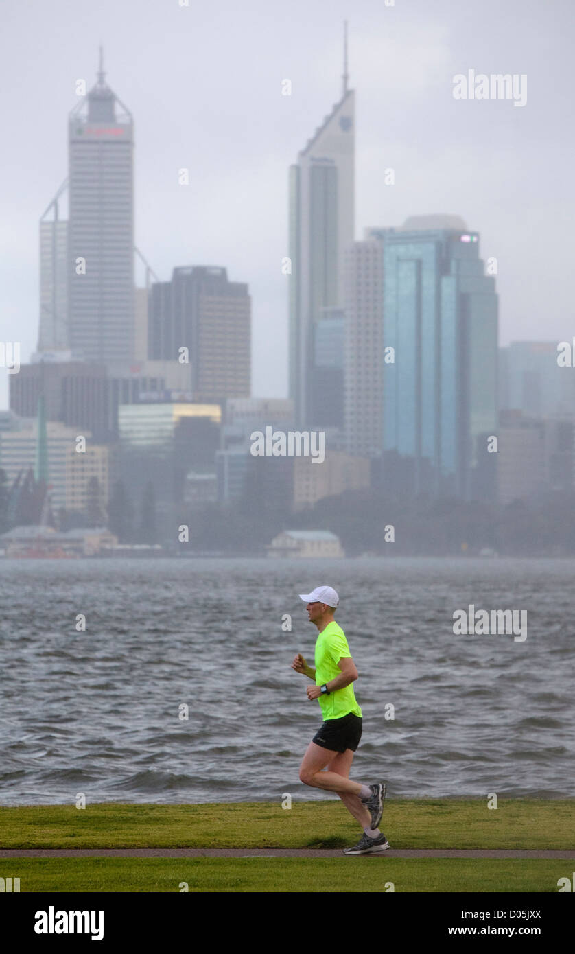 Un hombre corriendo en la lluvia con un río y la ciudad en el fondo. Foto de stock