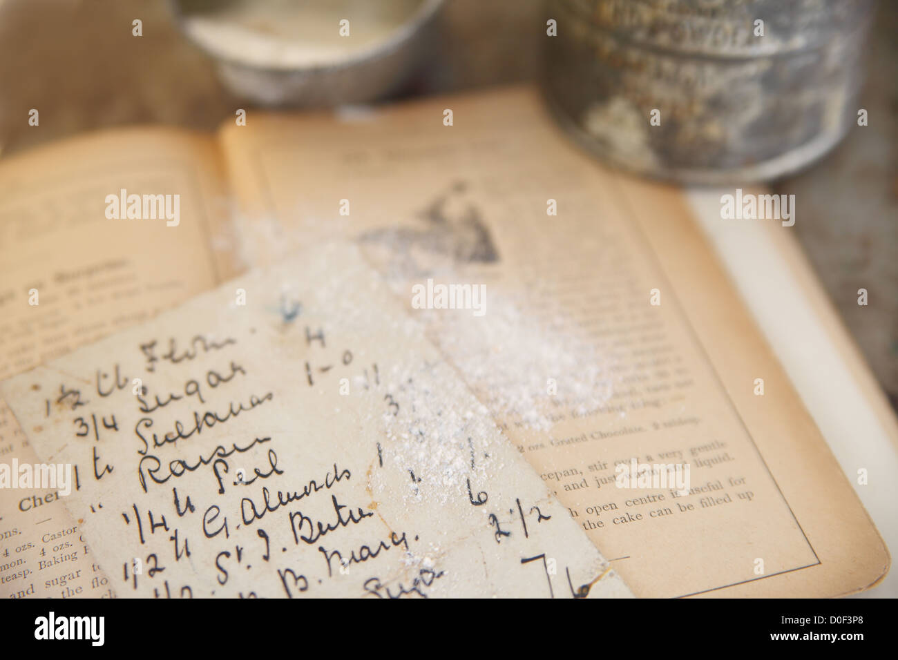 En la cima de una antigua receta cookbook desde 1894 espolvoreada con harina con el acribador del vintage y la taza de medir en segundo plano. Foto de stock
