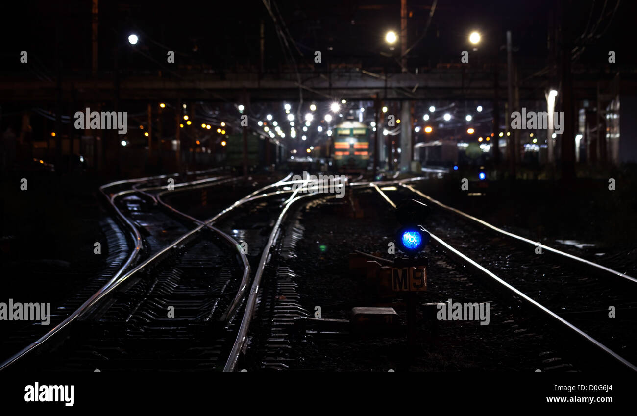 Railroad escena nocturna con semáforo azul y trenes de carga. El enfoque selectivo en semáforo Foto de stock