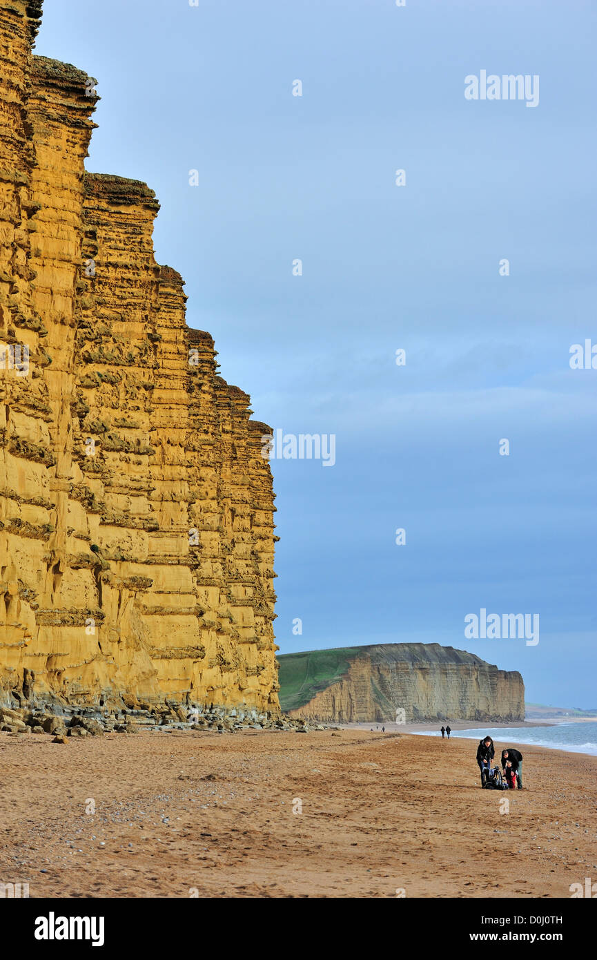 Paseantes caminando por la playa de East Cliff, hecha de piedra arenisca, cerca de West Bay a lo largo de la Costa Jurásica, en Dorset, en el sur de Inglaterra, Reino Unido. Foto de stock