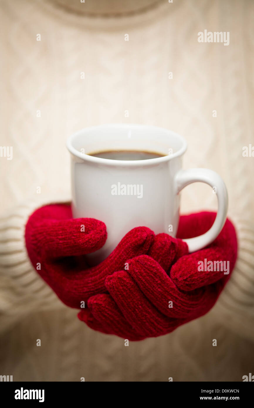 Mujer en un suéter rojo estacional mitones sosteniendo una taza de café caliente. Foto de stock