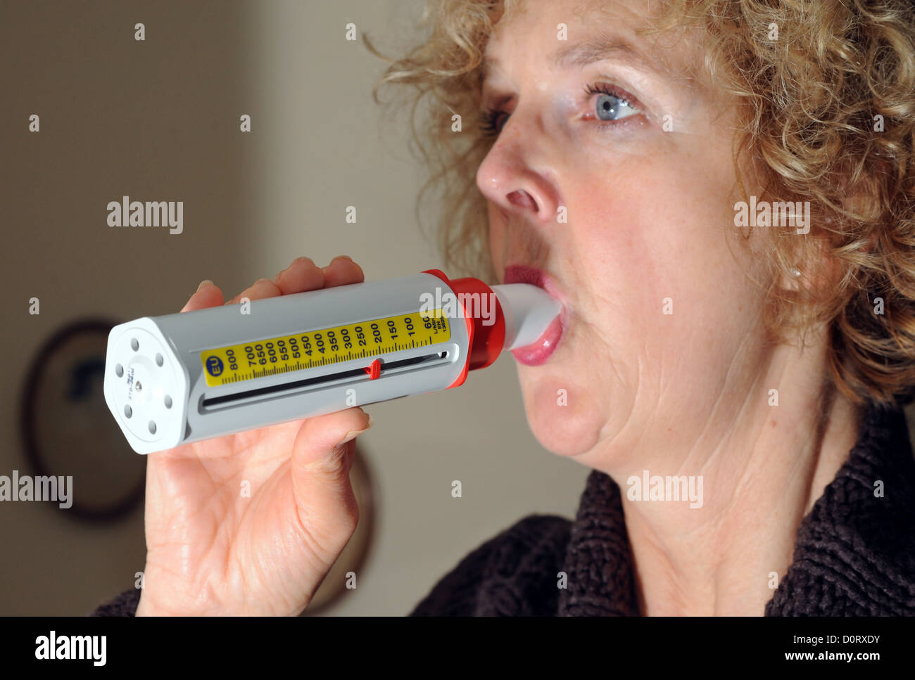 Mujer de mediana edad que sufre de asma en soplar dentro de un medidor de flujo pico tester . Foto de stock