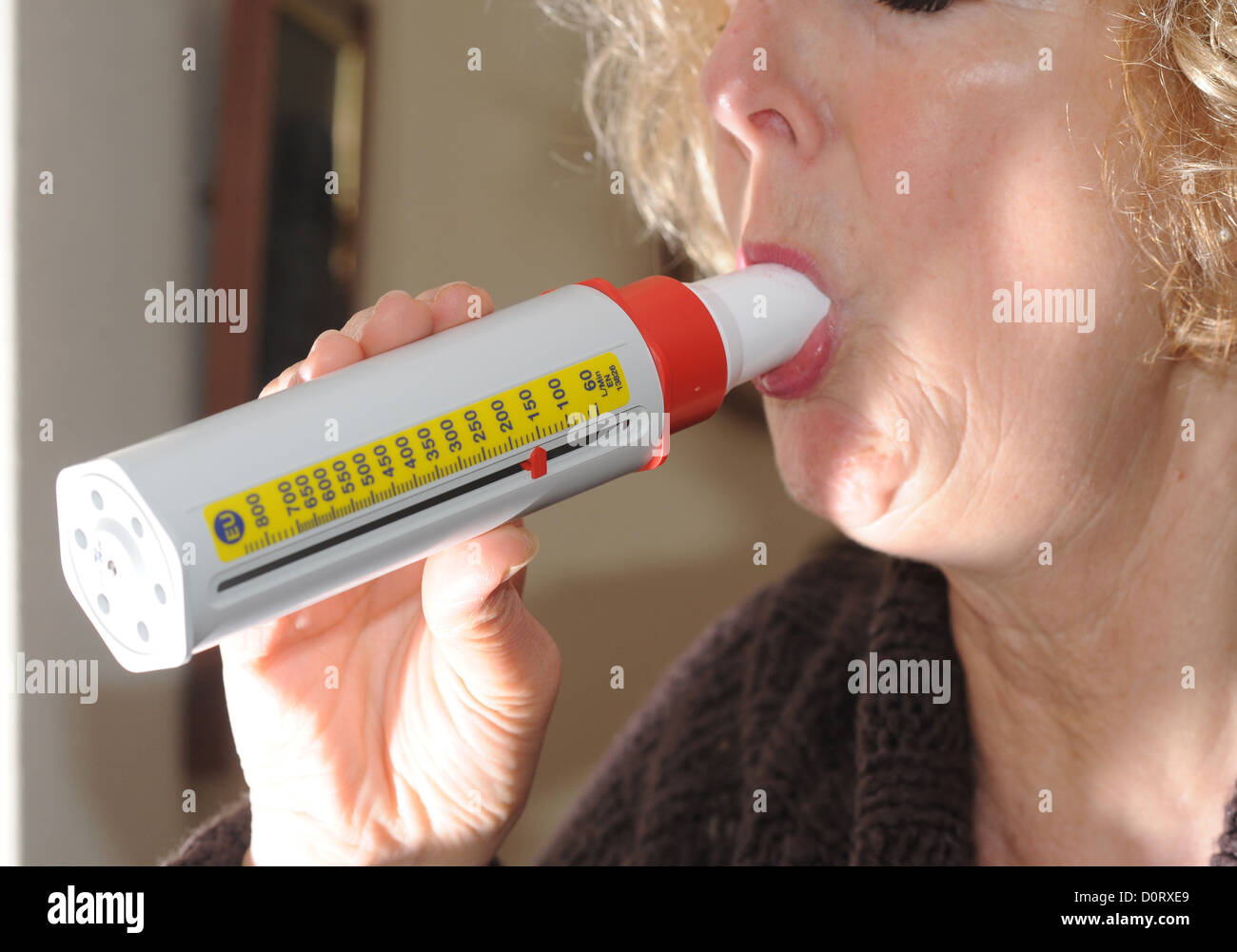 Mujer de mediana edad que sufre de asma en soplar dentro de un medidor de flujo pico tester . Foto de stock