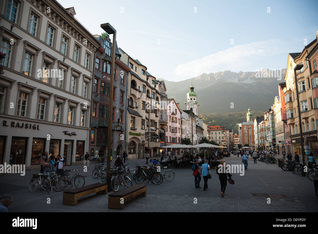 Mirando a Maria Theresien Strasse en Innsbruck a picos montañosos de los Alpes, personas para cenar fuera en la calurosa tarde de verano. Foto de stock