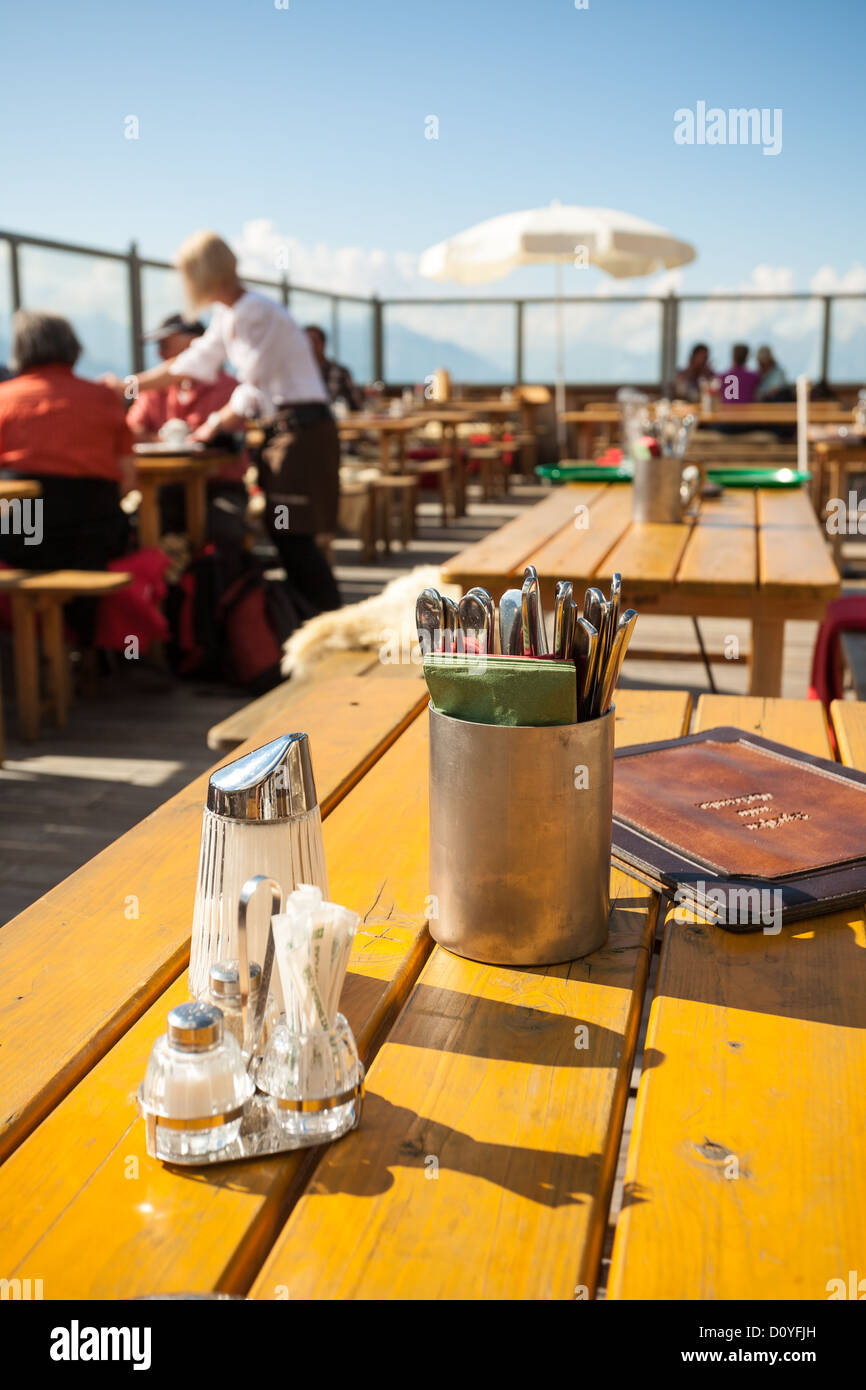 Camarera sirve mesas en un restaurante en la cubierta de el fuerte sol de verano tardío en la montaña Patscherkofel cerca de Innsbruck. Foto de stock