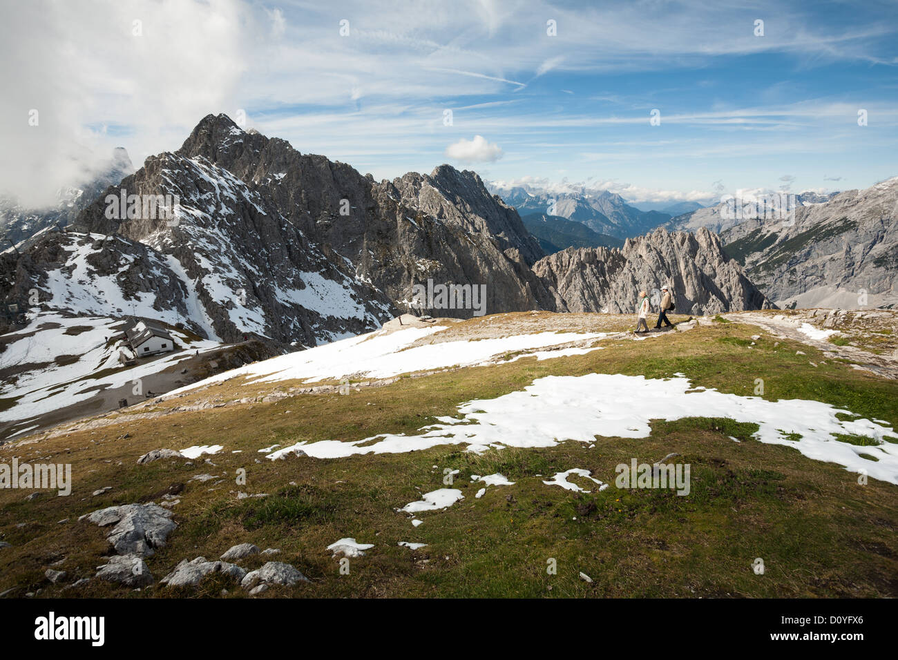 Pareja de turistas camina a través de la meseta de hierba con luz de nieve en los Alpes austríacos por encima de Innsbruck, con altos picos montañosos. Foto de stock