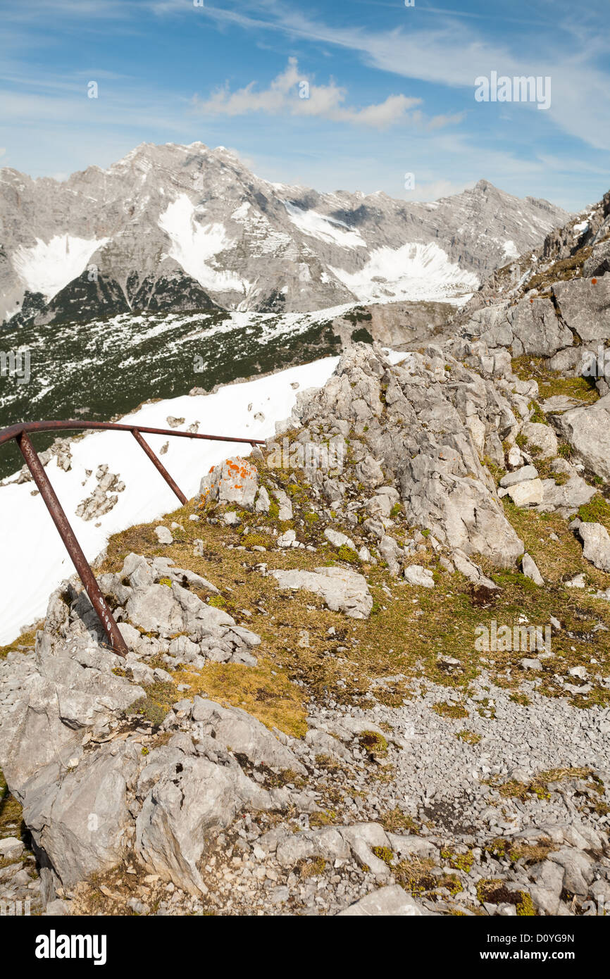 Antiguos pasamanos metálicos en el borde del acantilado rocoso en el Hafelekar pico en los Alpes austríacos, con ligera nieve y nublado cielo azul. Foto de stock