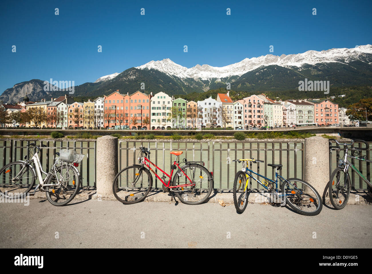 Bici recostada contra una valla, al otro lado del río la famosa Innsbruck coloridas casas con montañas cubiertas de nieve. Foto de stock