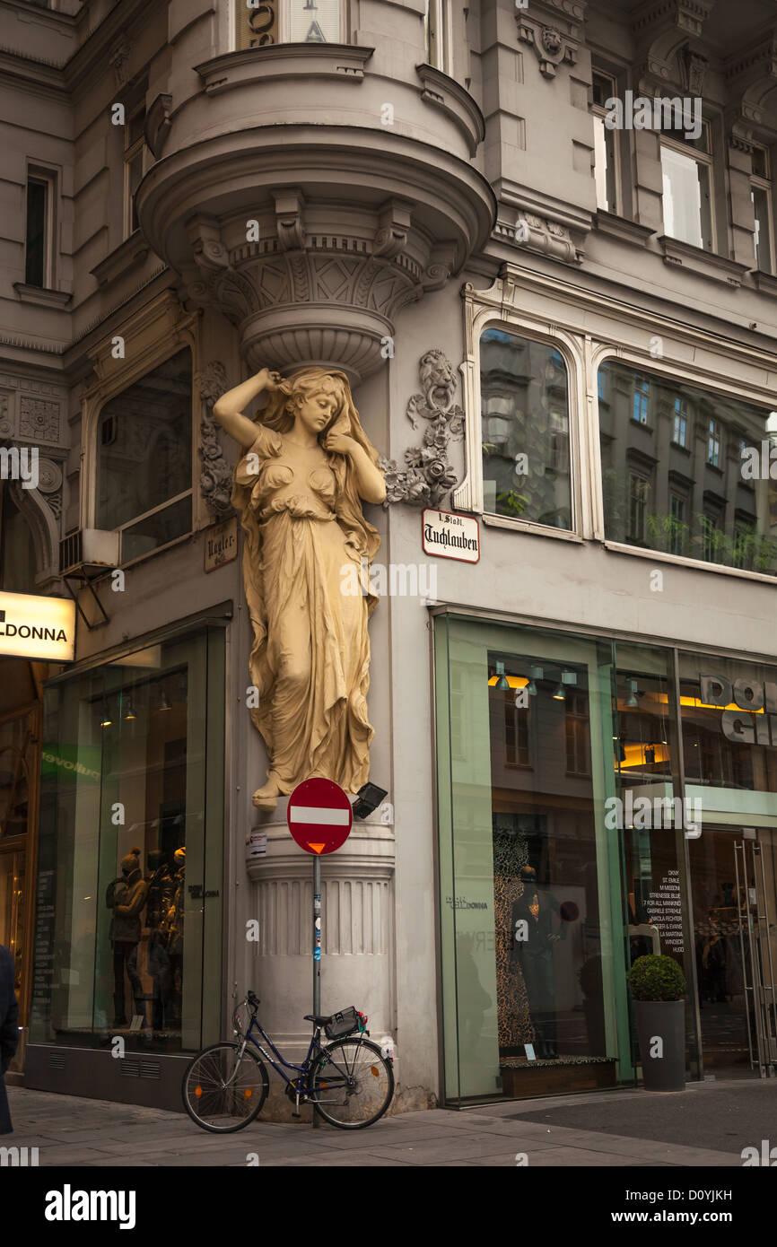 Bicicleta aparcado fuera de una tienda Art Deco debajo de una escultura de una mujer la celebración hasta la esquina de un edificio decorativo en Viena. Foto de stock