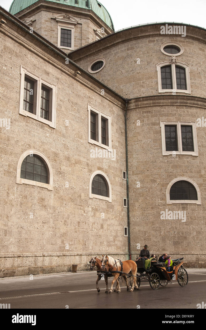 Un caballo y una carroza tiene familia de turistas para dar un paseo alrededor de Salzburgo Residenzplatz, pasando por las altas paredes de piedra de la Catedral. Foto de stock