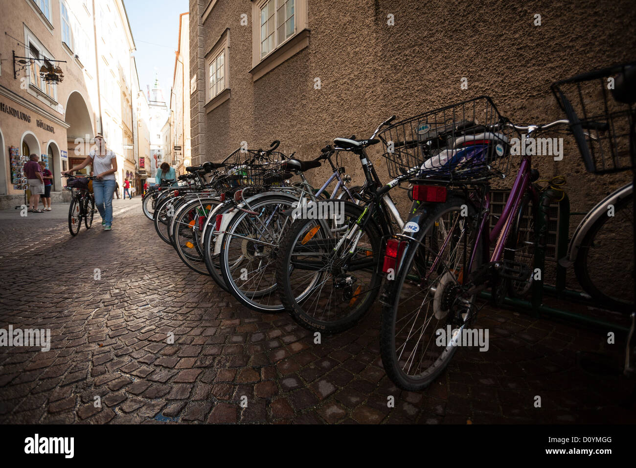 Mujer con bicicleta paseos por cobblestone lane, cerca de la Universidad de Salzburgo con motos aparcadas contra el muro de piedra. Foto de stock