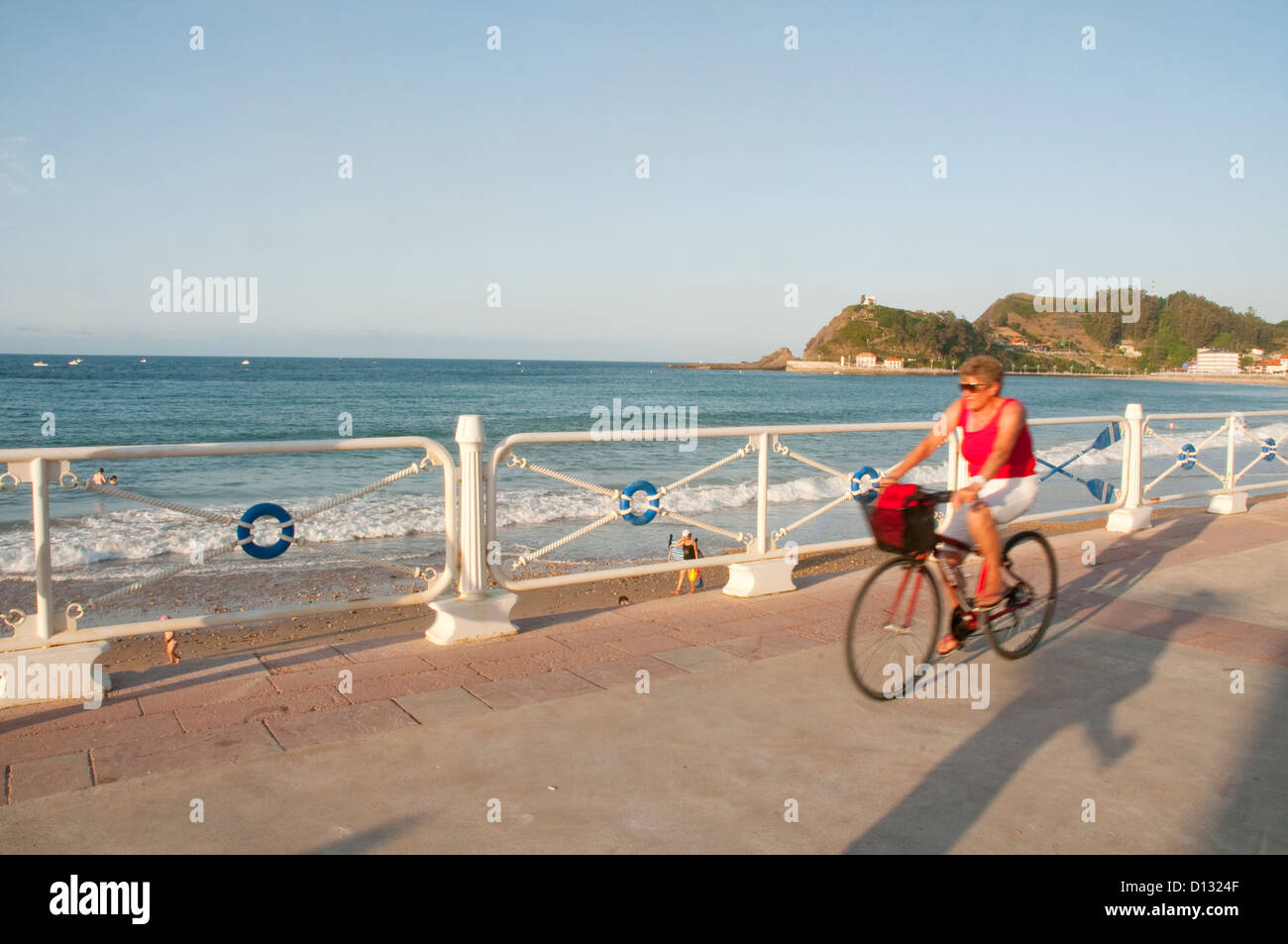 Mujer madura, montando en bicicleta por el paseo marítimo. Playa de Santa Marina, Ribadesella, Asturias, España. Foto de stock