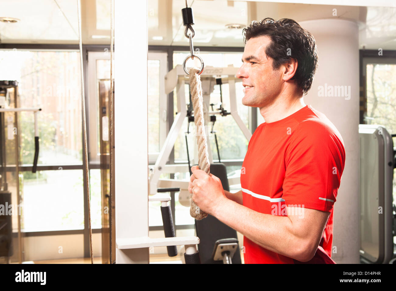 Hombre utilizando equipo de ejercicio en el gimnasio Foto de stock