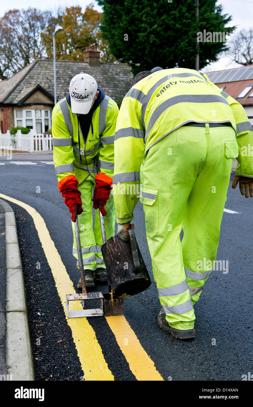 Los trabajadores de mantenimiento de carreteras, por la que se establecen las líneas amarillas dobles. Foto de stock