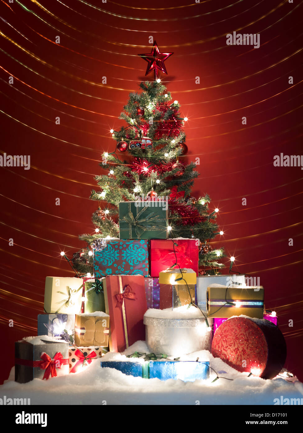 Árbol de navidad decorado con globos rojos, tinsels y estrella con una pila  de brillantes presenta delante de él cubierto con nieve, rodeada con  coloridas luces de Navidad Fotografía de stock -