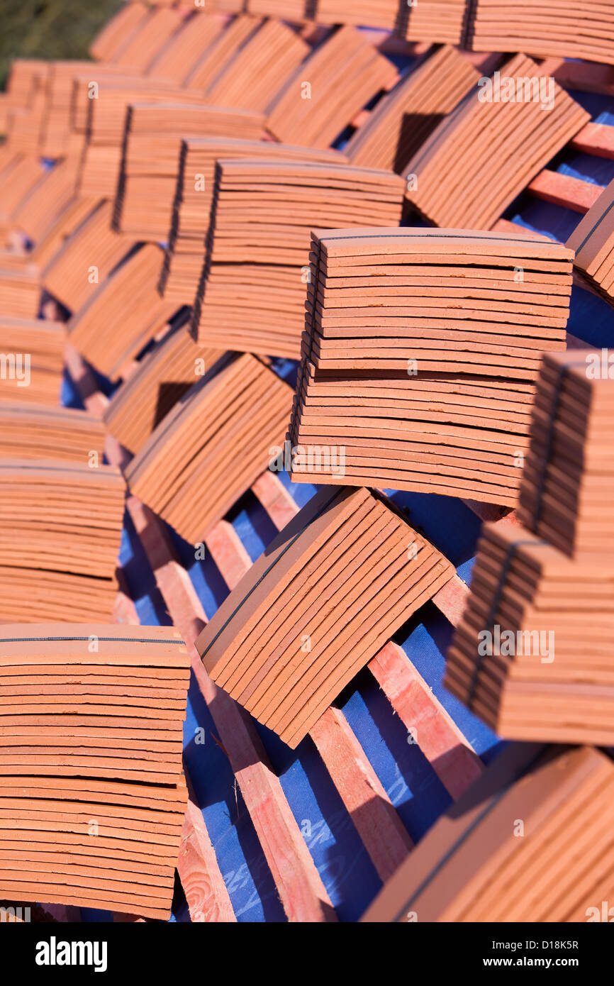 Pilas de techos de tejas rojas en equilibrio sobre un techo bajo construcción. Foto de stock