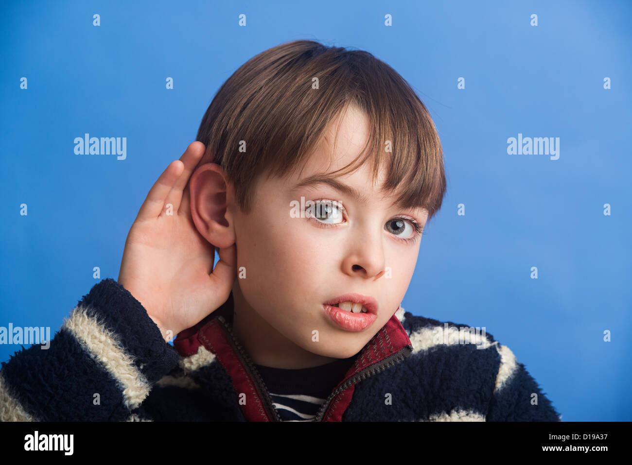 Niño de 8 años sobre un fondo azul de catación para mejorar la audición del oído. Que muestra el uso de la sensación de oír. Foto de stock
