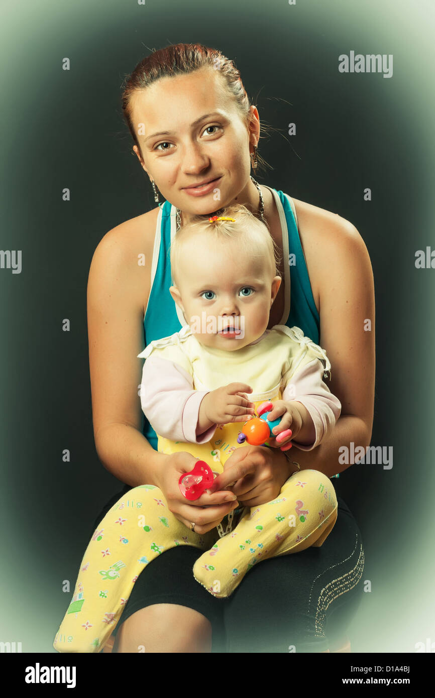 Hermosa caucásico buena madre sosteniendo a su hija en sus brazos sobre un fondo oscuro Foto de stock