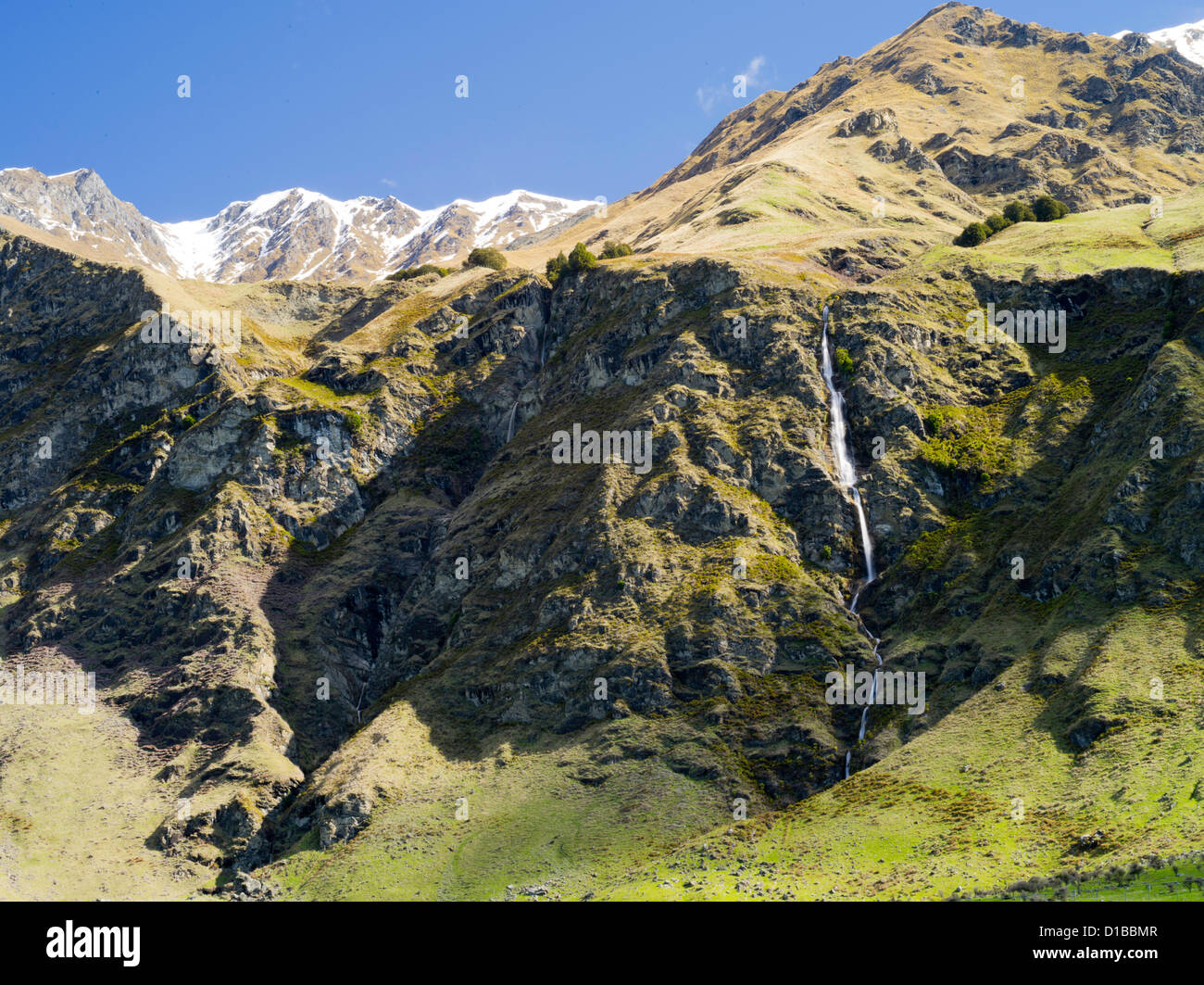 Una cascada fluye hacia abajo por una robusta montaña cerca de Treble Cone Ski Area, Harris Mountains, cerca de Wanaka, Nueva Zelanda Foto de stock