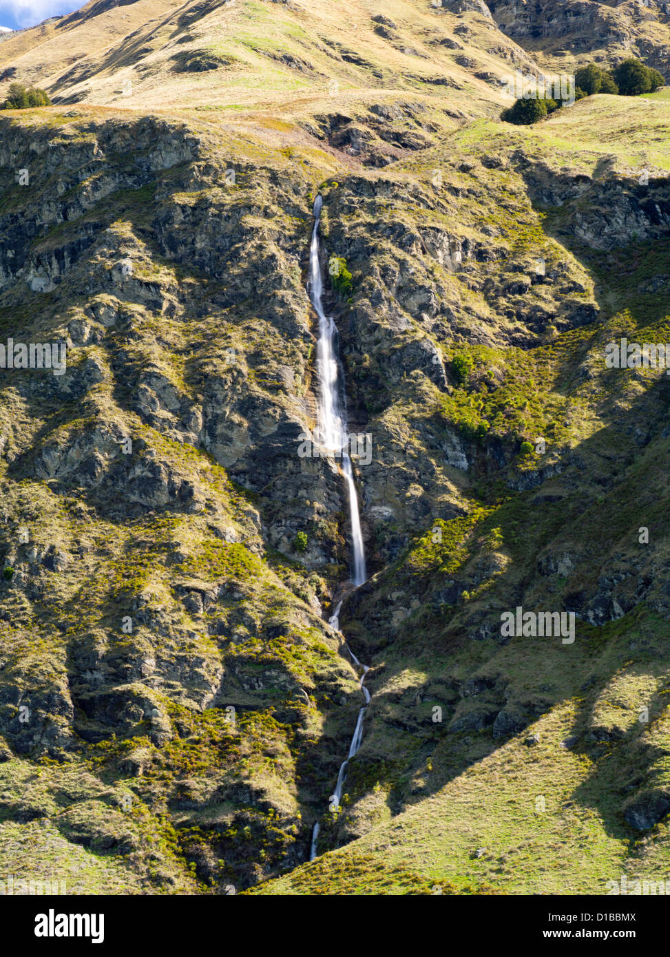 Una cascada fluye hacia abajo por una robusta montaña cerca de Treble Cone Ski Area, Harris Mountains, cerca de Wanaka, Nueva Zelanda Foto de stock