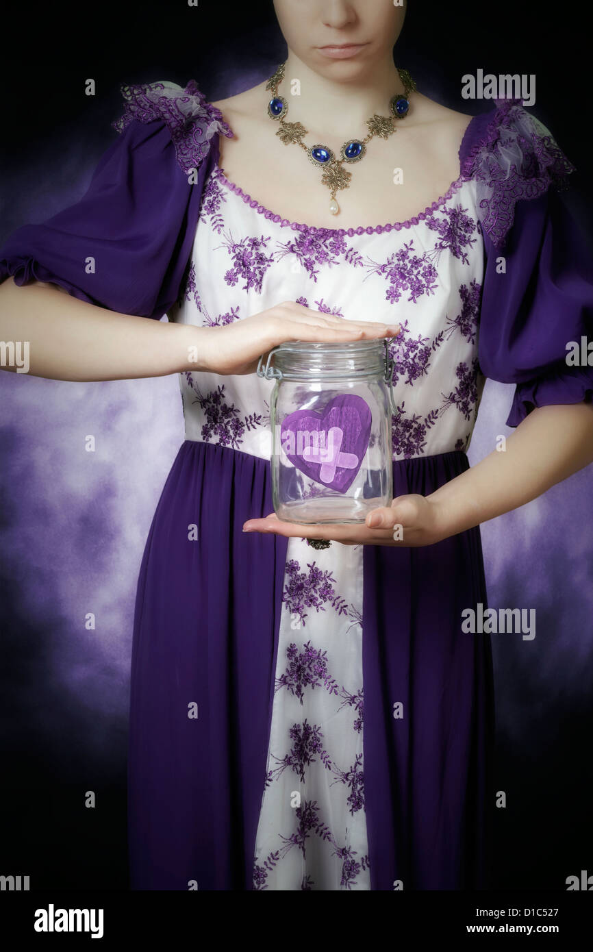 Una mujer en un período vestido está sosteniendo un frasco con un corazón roto Foto de stock
