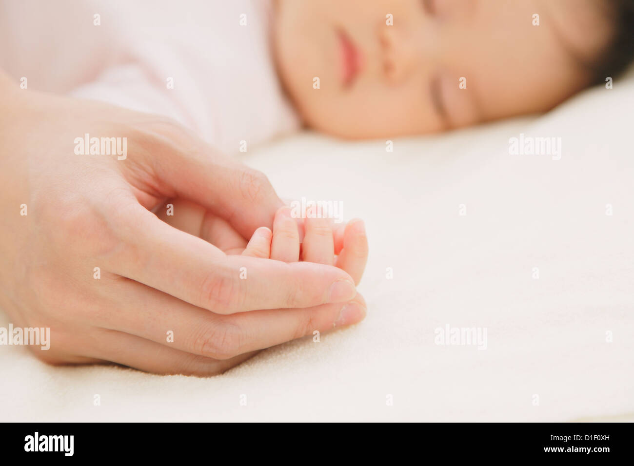 Baby Boy durmiendo en cama y las manos de su madre Foto de stock