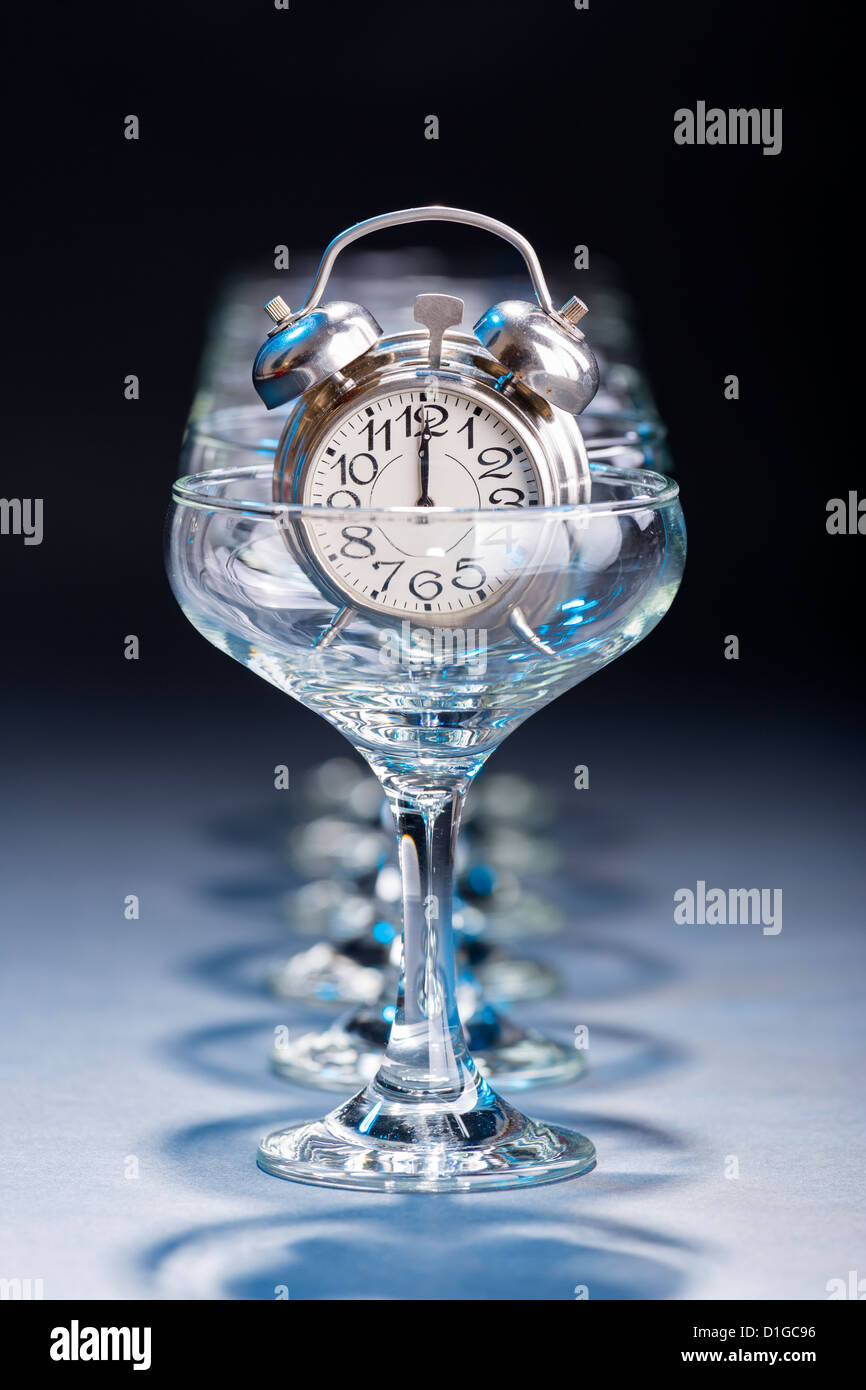 Reloj de alarma en una copa de champán vacía mostrando las doce horas. Foto de stock
