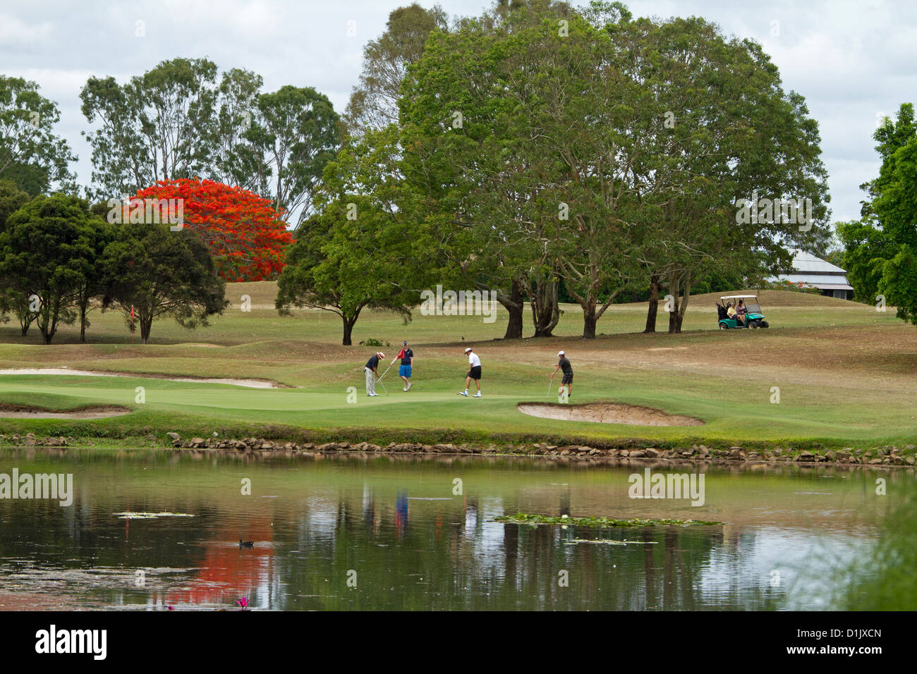 Grupo de golfistas jugando junto al lago, en el pintoresco campo de golf con los árboles y las personas se refleja en el agua Foto de stock