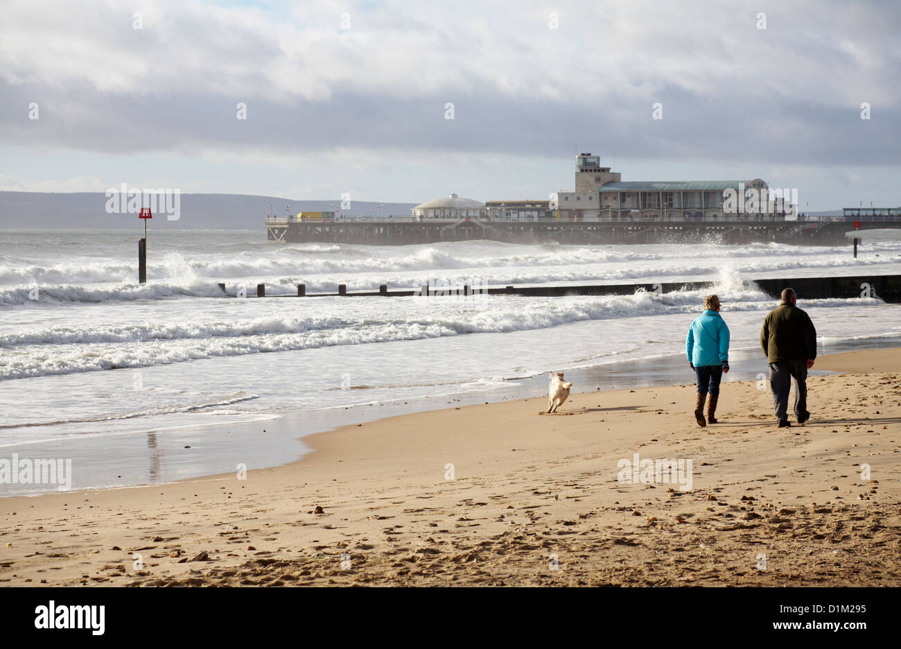 Pareja paseando a un perro a lo largo de la playa de Bournemouth hacia el muelle de Bournemouth en el día de Navidad. Foto de stock