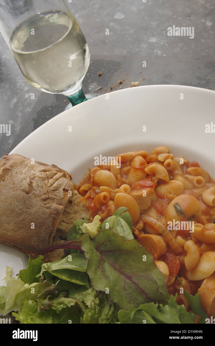 Las pastas italianas y judías con ensalada y pan en la placa blanca, servido con un vaso de vino blanco seco Foto de stock