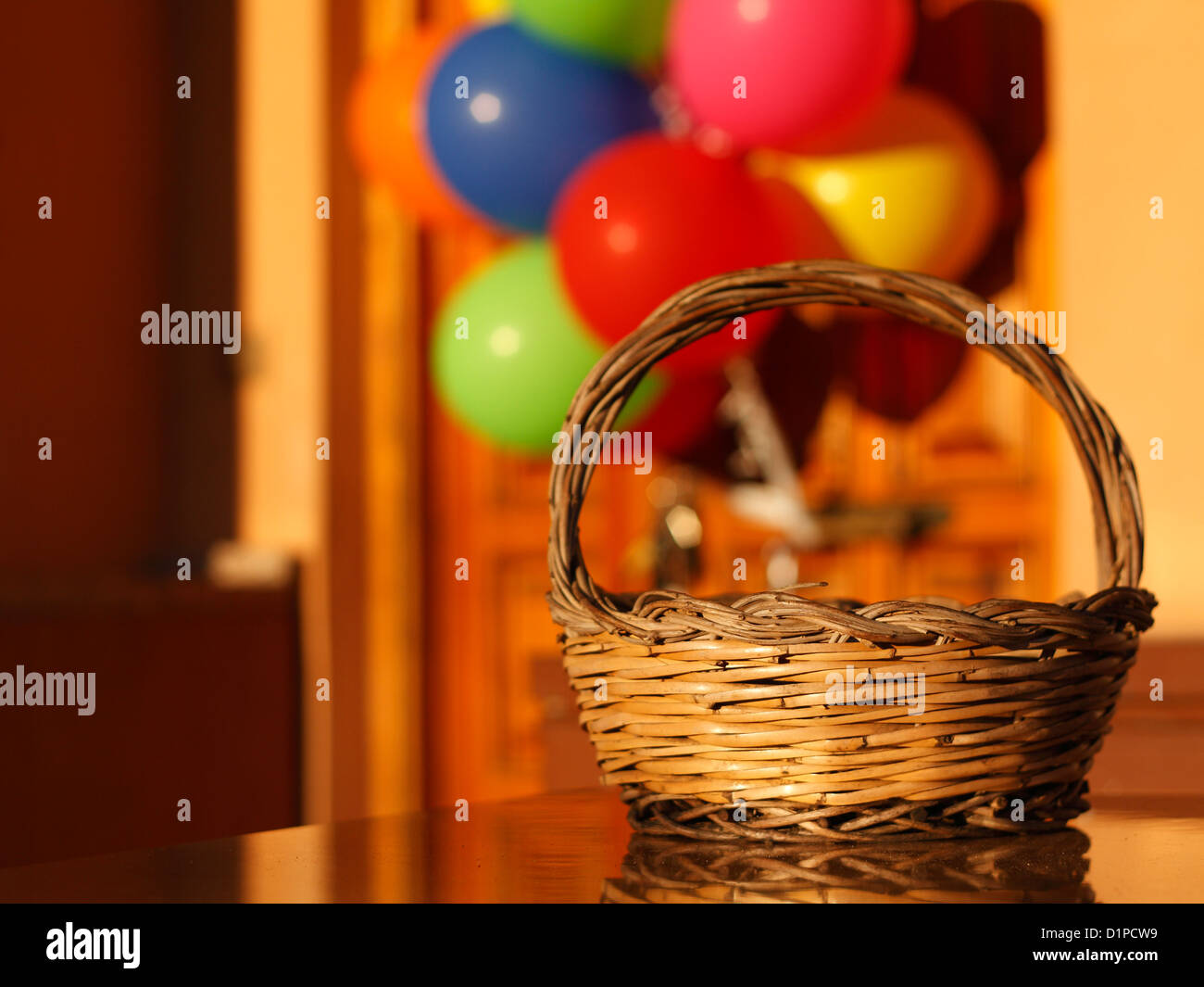 Una cesta de mimbre en frente de una puerta con globos en fuera de foco. Foto de stock