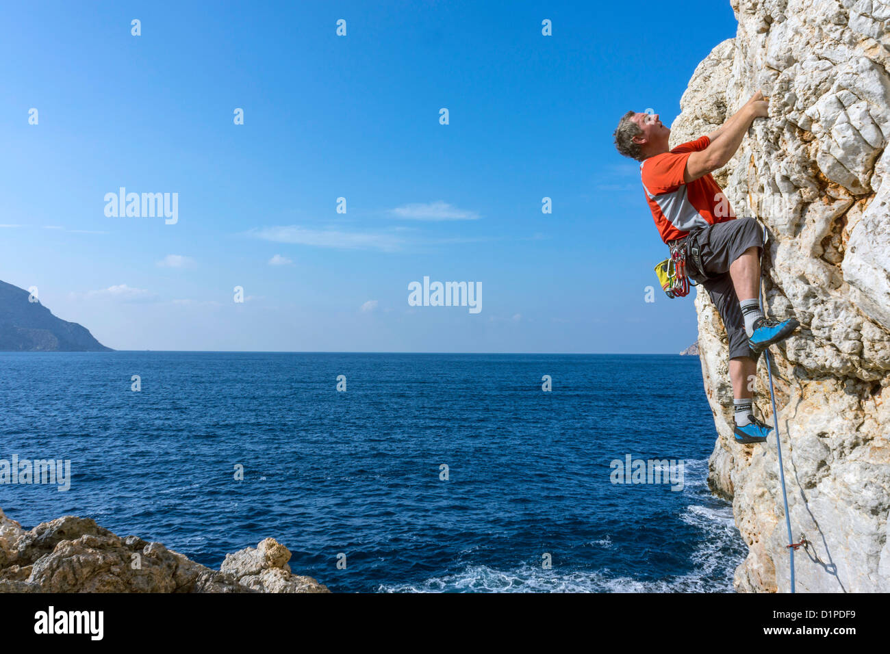 Escalador masculino vestidos de rojo sobre el acantilado, Kalymnos, Grecia Foto de stock