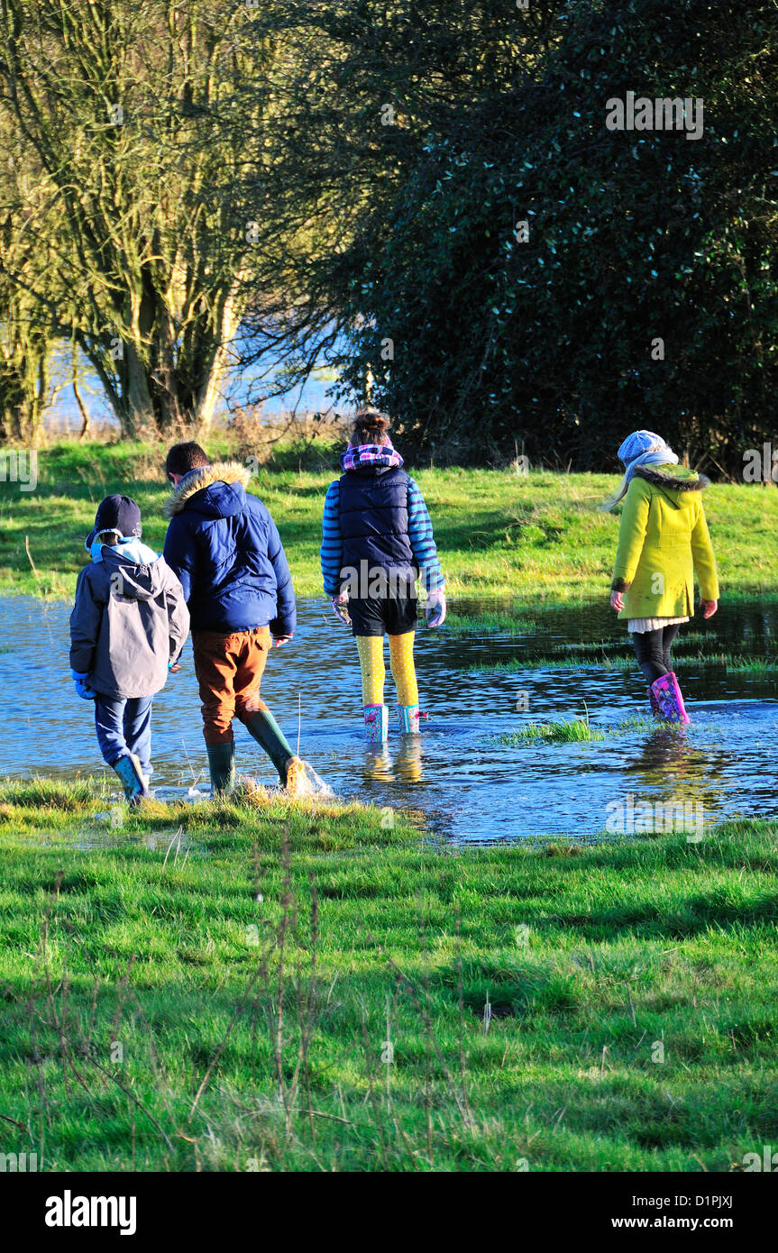 Cuatro niños (vista trasera) en un día de Año Nuevo caminar junto al río inundado Windrush , entre Burford y Swinbrook, Cotswolds, Oxon,UK Foto de stock