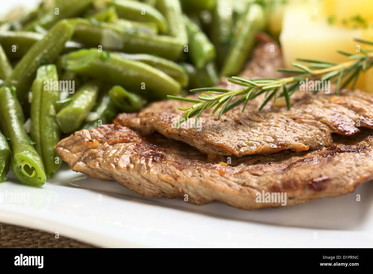 Cortes de carne de vacuno con romero fresco encima, servido con judías verdes y patatas cocidas Foto de stock