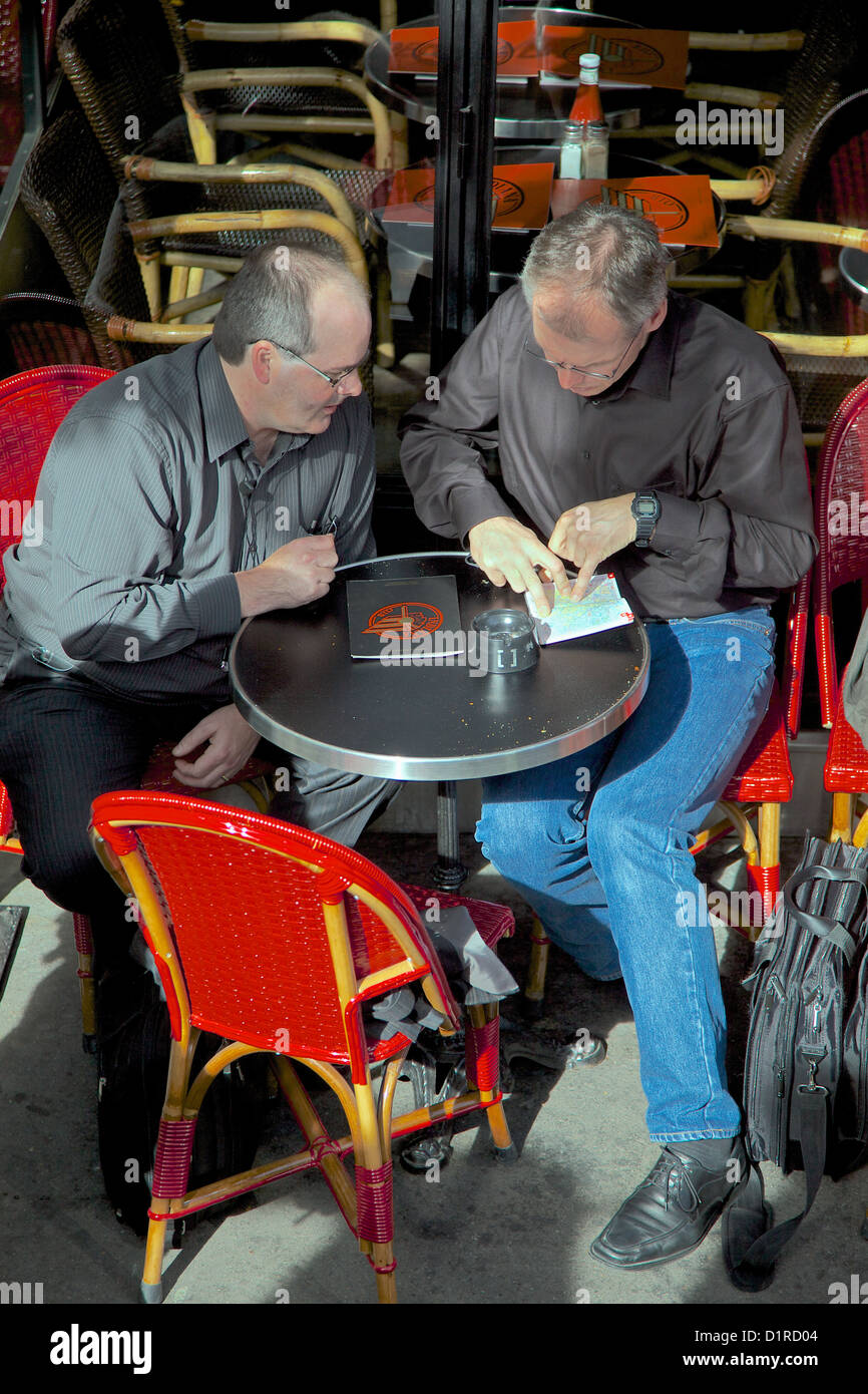 Dos hombres se sientan en una mesa de café de París estudiando un mapa y direcciones Foto de stock